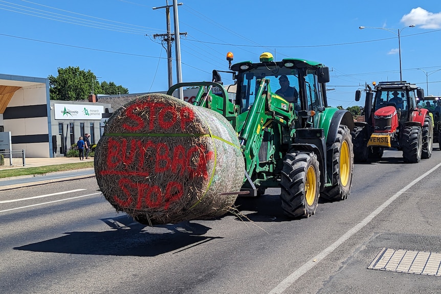 A tractor driving in Shepparton as part of a convoy carrying a hay bale that has the words "stop buyback stop" painted on it.