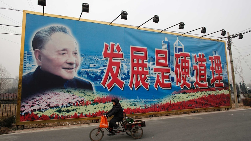 A woman rides a tricycle past a giant poster of late Chinese leader Deng Xiaoping.