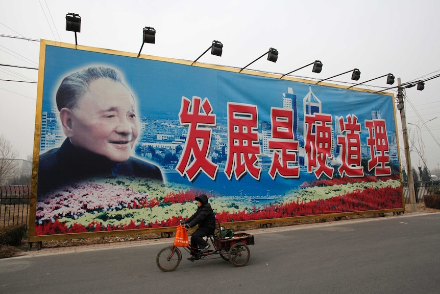 Une femme conduit un tricycle devant une affiche géante du défunt leader chinois Deng Xiaoping.