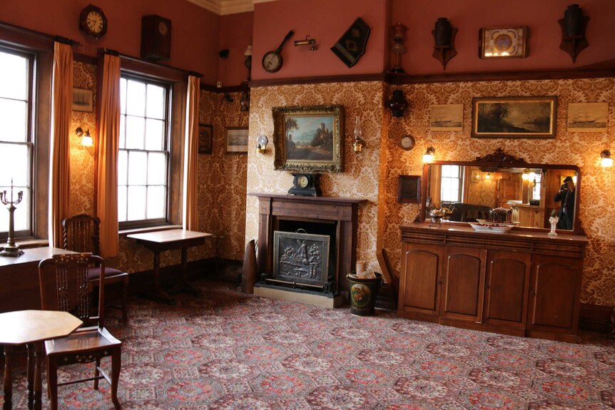 The interior of a historic pub with carpet, wallpaper, heavy curtains and wooden furniture