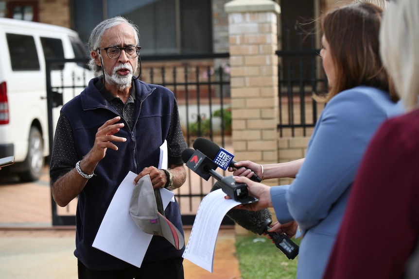 A man talks to reporters outside a house.
