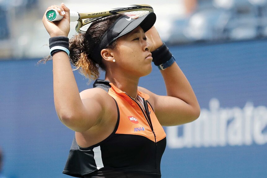Naomi Osaka holds her racquet in both hands across the top of her head