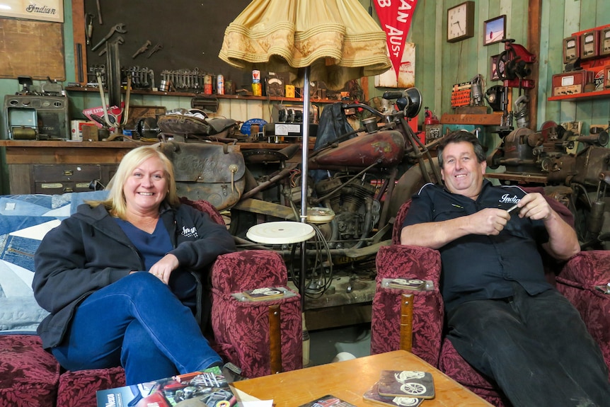Toni and Peter sit in vintage arm chairs in their museum which is decked out  to look like a 1920s store