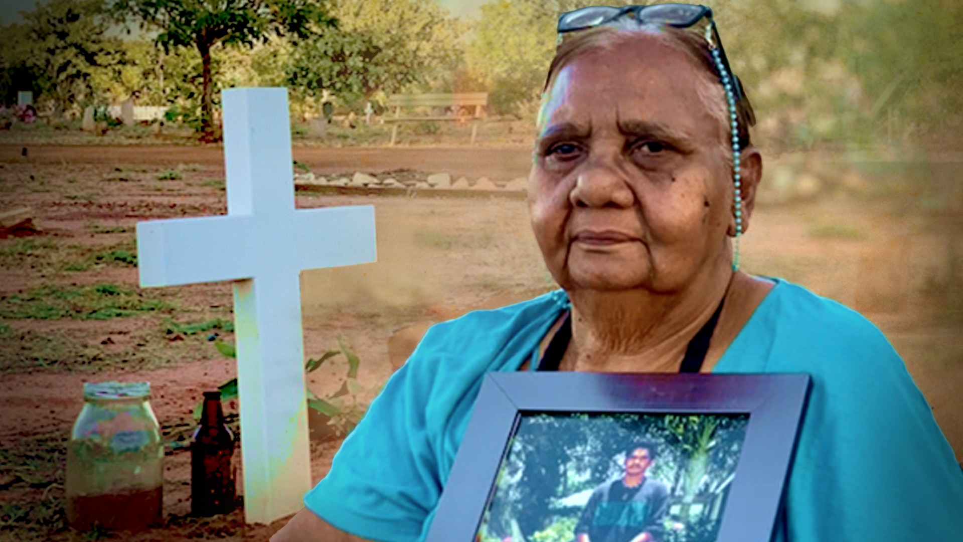 A woman in a blue short holding a photograph of a young Aboriginal man