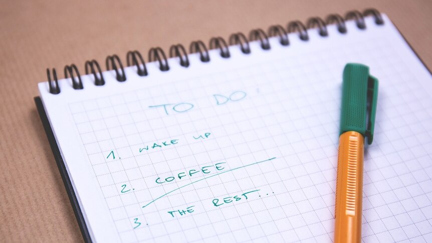 A spiral notebook with a green pen on top. Words written: To Do, Wake Up, Coffee, The Rest...