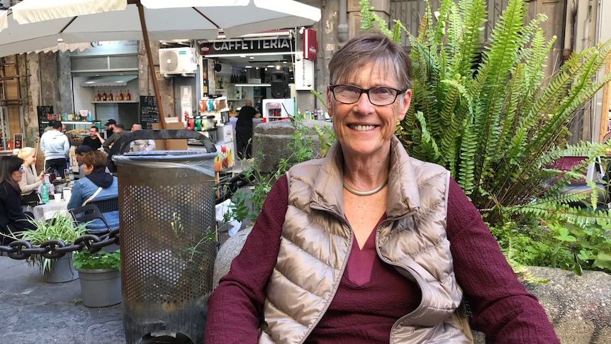 Mimi Ermert smiles while sitting in front of a streetfront cafe.