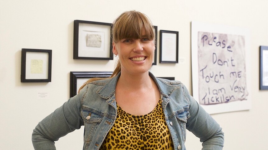Medium portrait shot of a woman standing in an art gallery smiling at the camera.