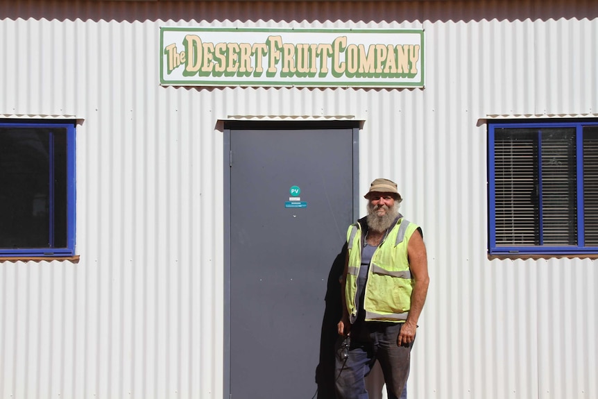 A man standing outside a shed with a sign saying "The Desert Fruit Company".