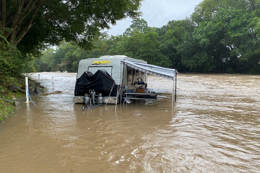 A caravan with its wheels covered in floodwaters.