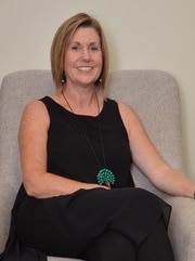 A woman in a black dress is sitting in a chair and smiling at the camera