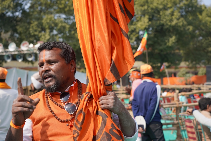 Indian man wearing orange, holding a flag. 