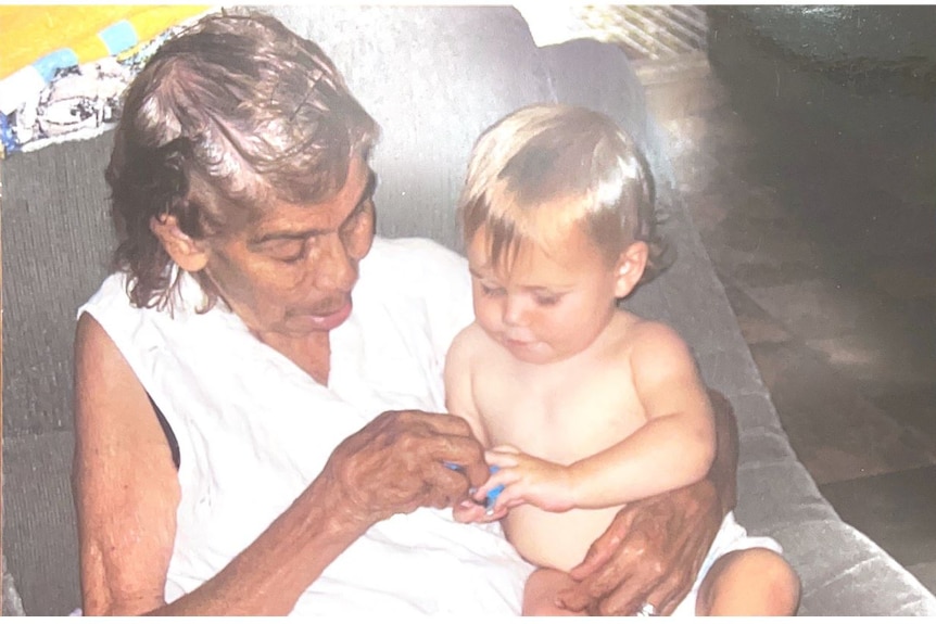 Изображение на Нида Лоу, седнала с внука си Хъдсън в скута си, държейки ръцете му и усмихната