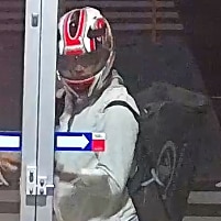 A still image taken from CCTV footage showing a burglar standing at a door with a bike helmet on and bag on their back.