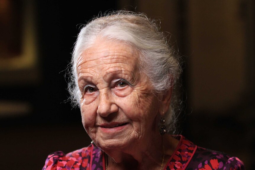 An old woman with white hair looks towards the camera.