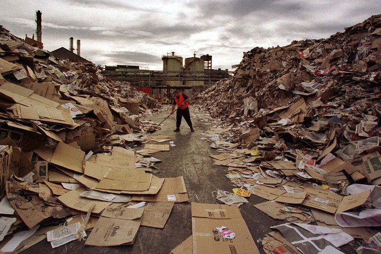 Man in high-vis vest sweeps cardboard pile