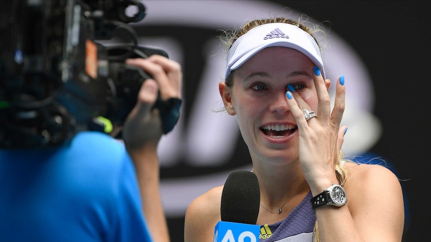 A tennis player looks away and brushes tears from her eyes after her final career match.