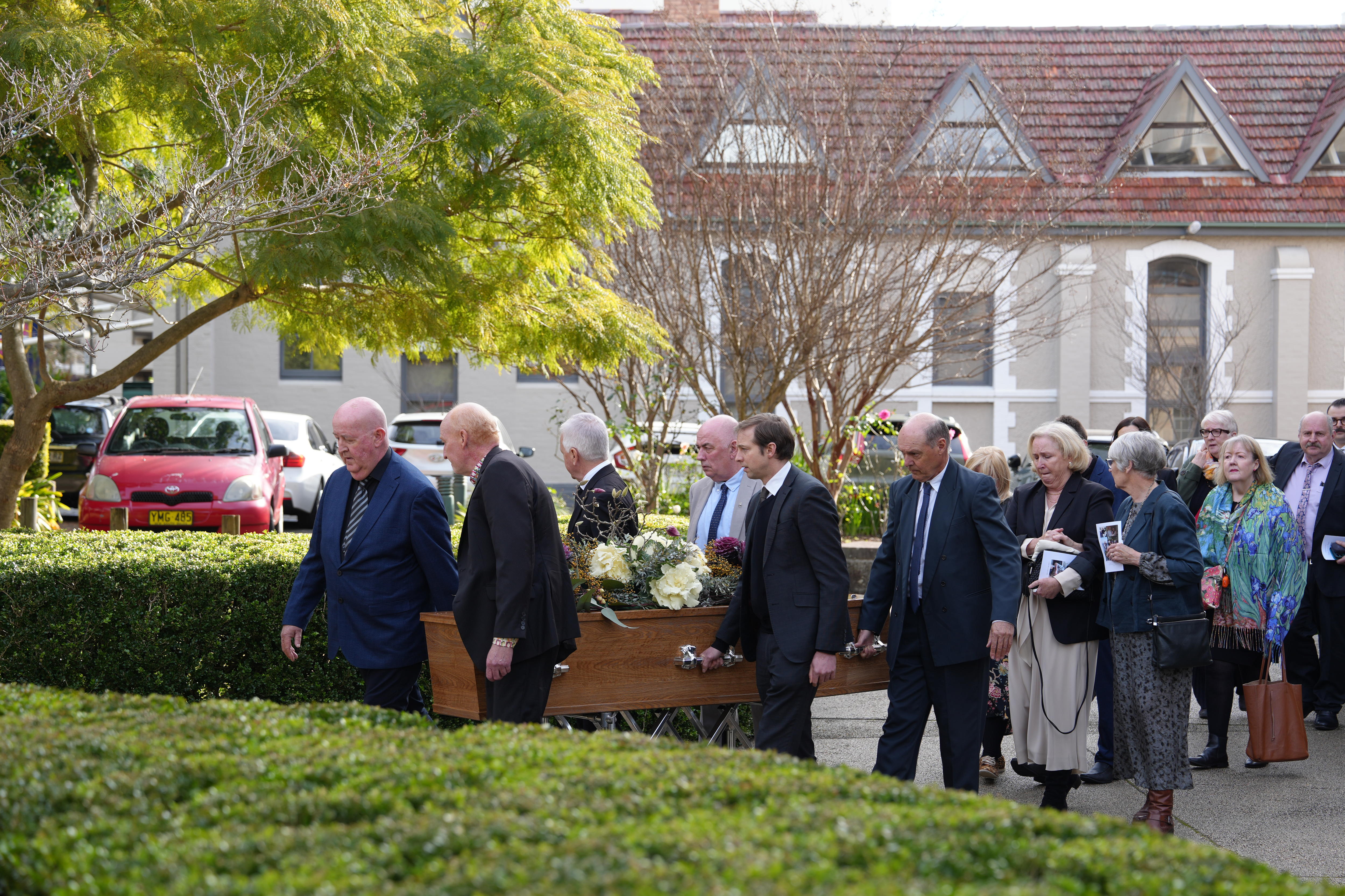 A group of people lead away a casket, outside a funeral.