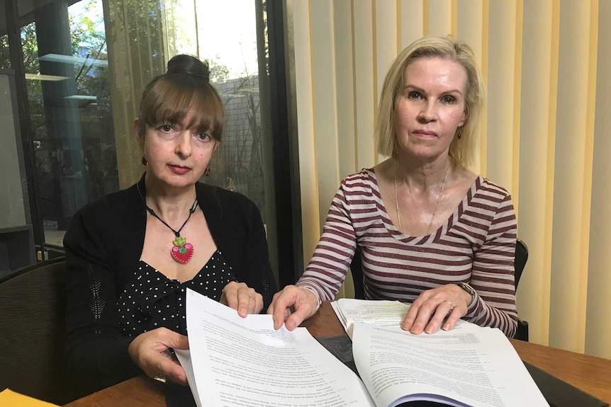 Two women sit down and look at the camera.