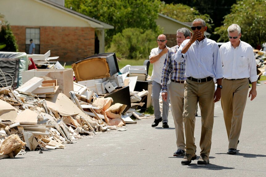 Barack Obama holds his hand over his mouth as he walks past debris left by flooding in Louisiana.
