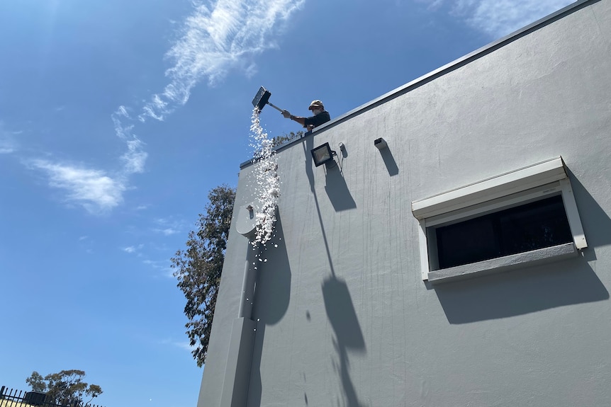 A person throws hail from the roof of a modern building using a shovel