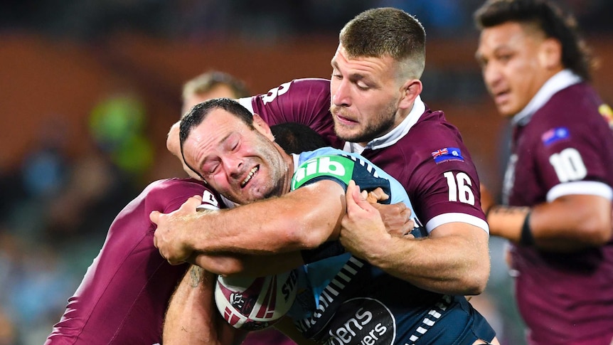 A NSW forward grimaces as he is held in a tackle by an opposition forward in State of Origin.