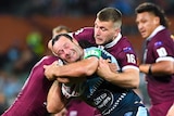 A NSW forward grimaces as he is held in a tackle by an opposition forward in State of Origin.