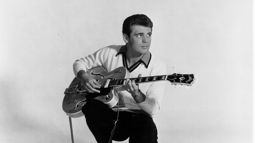 black and white photo of guitarist duane eddy crouching and holding a hollow body electric guitar