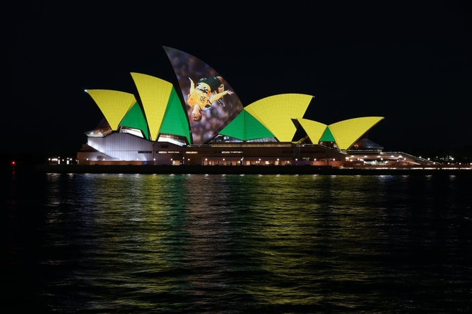 the opera house sails are lit up in green and gold. the centre sail bears a photo of Sam Kerr mid-backflip.