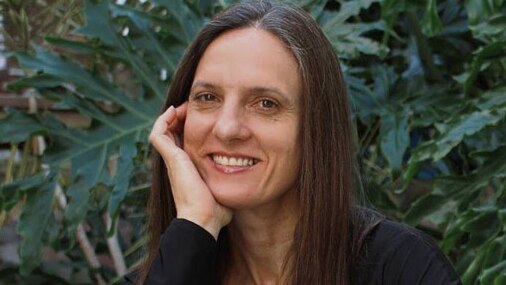 A woman with long brown hair and a black top smiles for the camera.