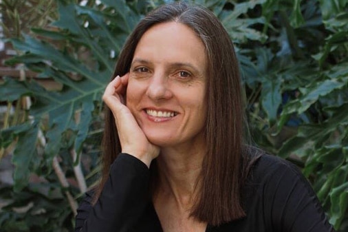 A woman with long brown hair and a black top smiles for the camera.