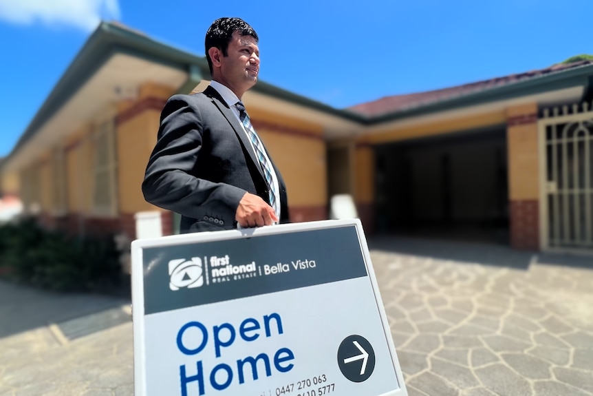 Real estate agent Tanmay Goswami carries an open home sign.
