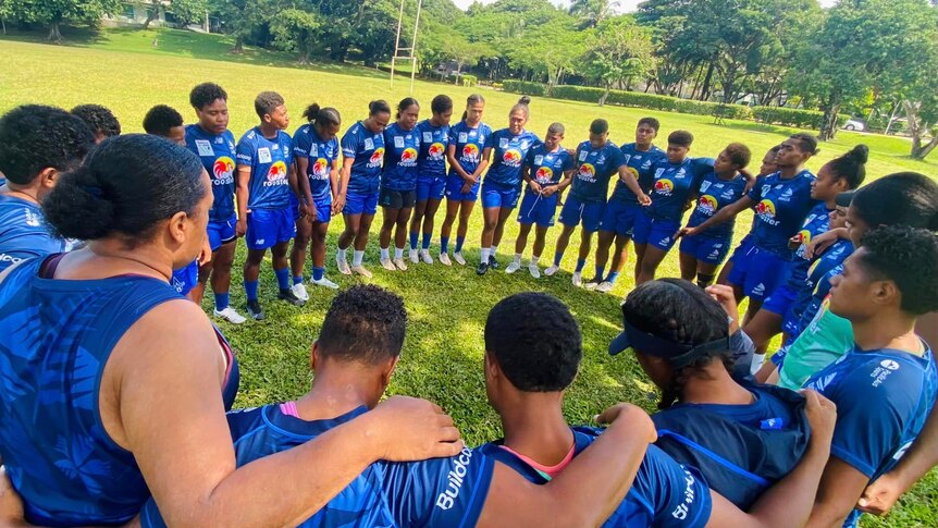 Women in rugby training gear form circle to prayer on rugby oval in Fiji 