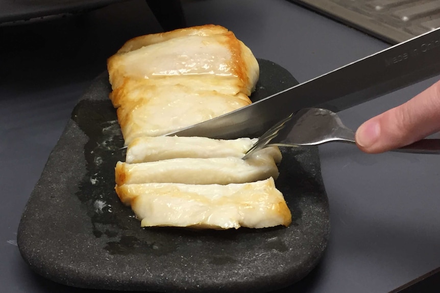 Crocodile steak on a plate, being cut with knife