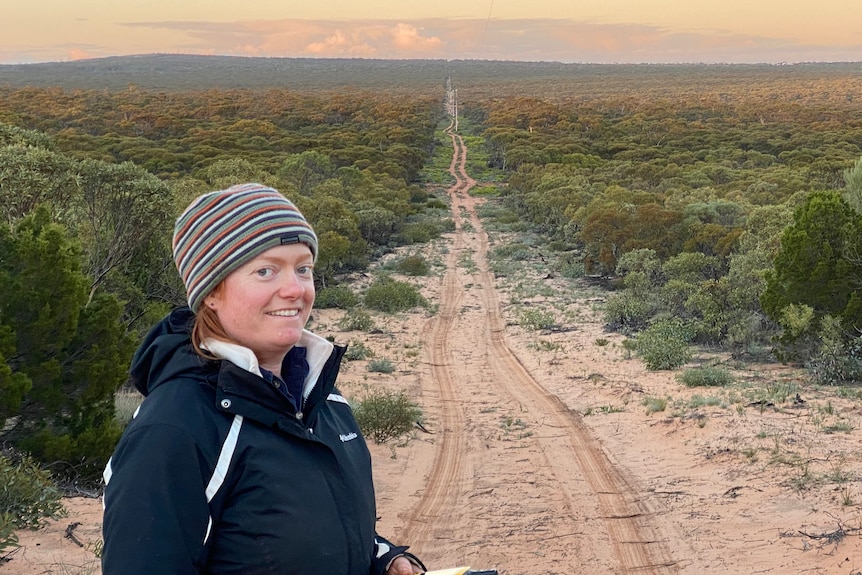 A woman smiles in front of a dirt road.