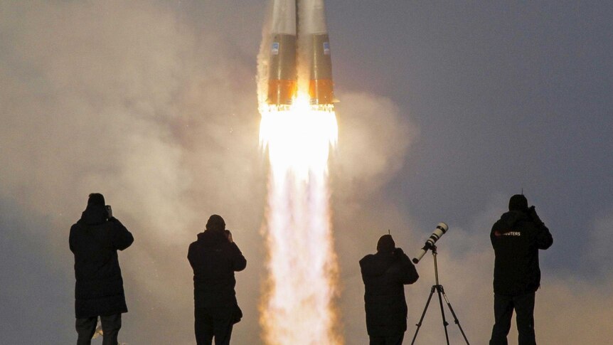 Four photographers are silhouetted as the Soyuz rocket takes off in the distance.