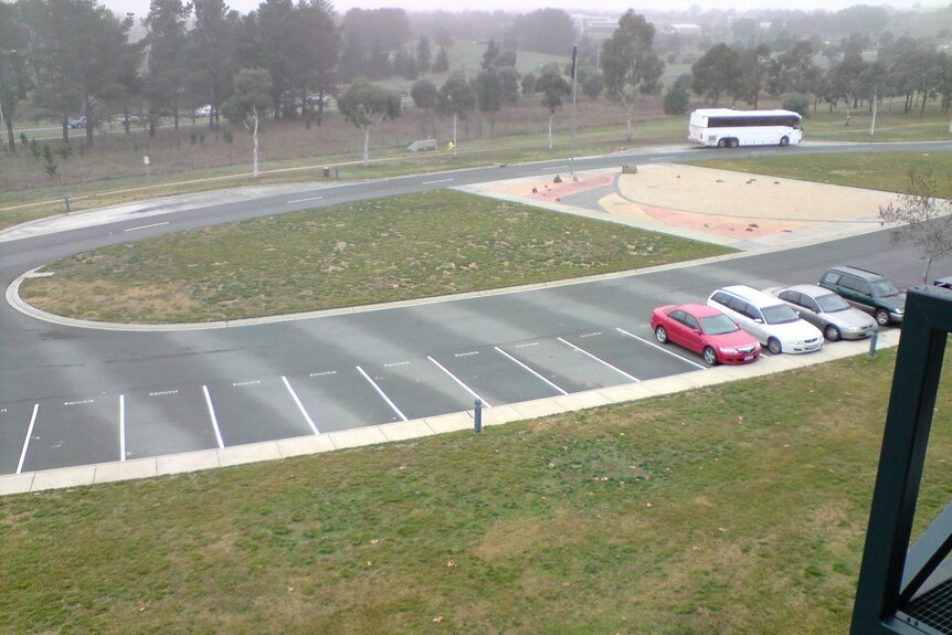 A damp carpark with strips of dry pavement, corresponding to the underground pipes.