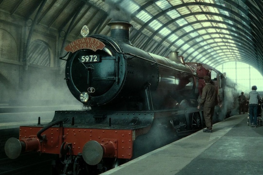 The Hogwarts Express at the train station with passengers preparing to board the train.
