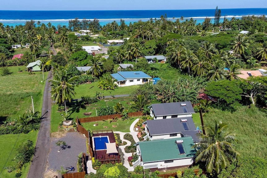 Bird's-eye view of white houses in lush, verdant setting and bright blue ocean in the distance.