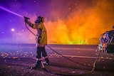 DFES firefighter holds a hose as embers fall around him, fire in background