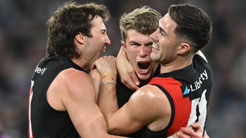 Three Bombers' AFL players embrace as they celebrate during their win over the Magpies.