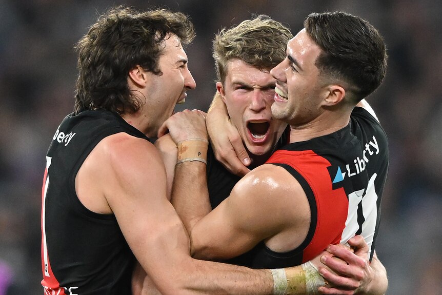 Three Bombers' AFL players embrace as they celebrate during their win over the Magpies.