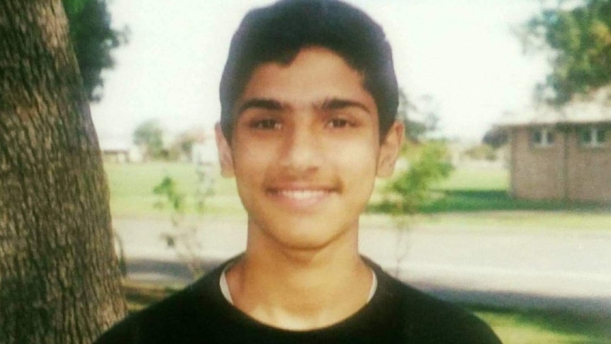 A faded photo of a teenaged boy posing in front of a tree and smiling