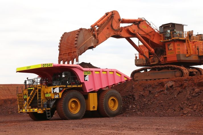 Une excavatrice chargeant un camion de minerai de fer rose dans la terre rouge du Pilbara.