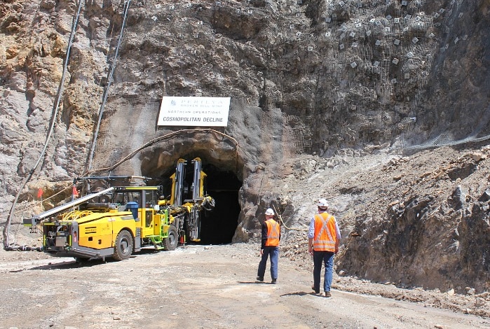 Workers in high vis at a cliff face on a mine site with a yellow mining vehicle.