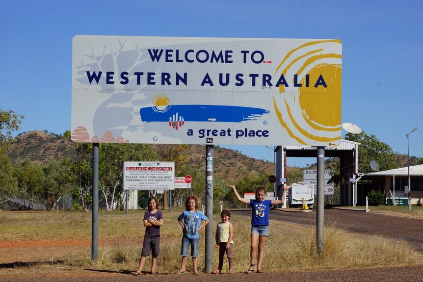 Four children stand under a 'Welcome to Western Australia' sign.