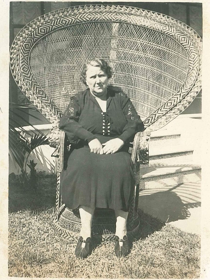 An older woman sits in a large wicker chair. Black and white photo.