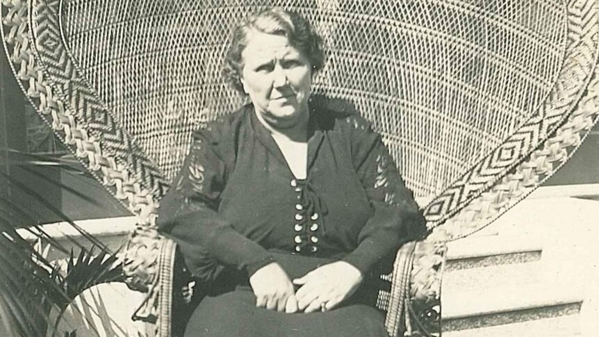 An older woman sits in a large wicker chair. Black and white photo.