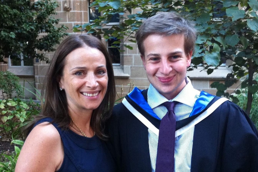 Samuel Symons stands next to his mother wearing a graduation gown
