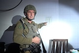 A man wearing military garb with weapons pointing at a piece of paper on the wall.
