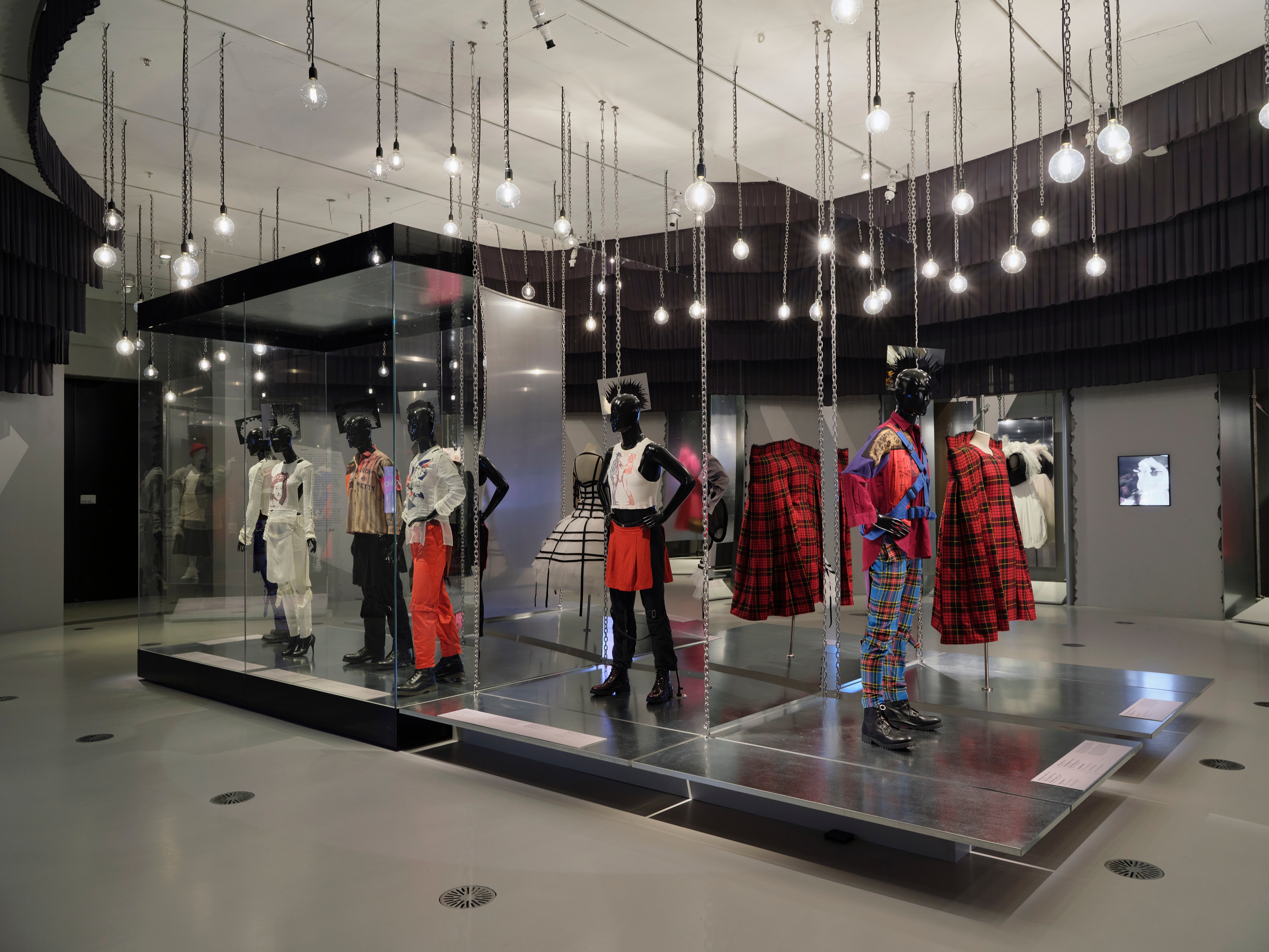 Foto de exposición de algunos maniquíes punk con faldas escocesas y camisetas rotas, mucho tartán.